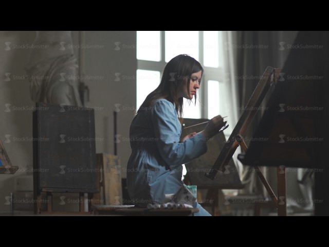 A woman painter paints behind an easel on canvas